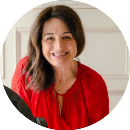 A woman with shoulder-length dark hair, wearing a red blouse, is smiling at the camera. The photo is set against a light-colored background and is cropped into a circular frame.