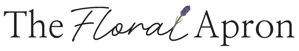 Logo reading "The Floral Apron" in elegant script, with the word "Floral" in cursive and a lavender sprig replacing the letter "l" in "Floral." The rest of the text is in serif font.