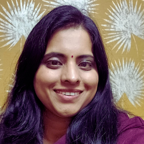 Smiling woman with long black hair, wearing a bindi, and a maroon top against a yellow background with white abstract patterns.