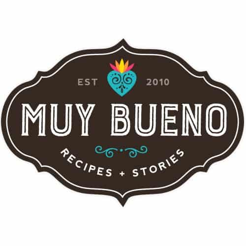 Logo of "Muy Bueno" featuring a decorative border. At the top, a colorful heart with a flame-like design. Text reads: "EST 2010," followed by "MUY BUENO" and "RECIPES + STORIES" below, in a vintage-style font.